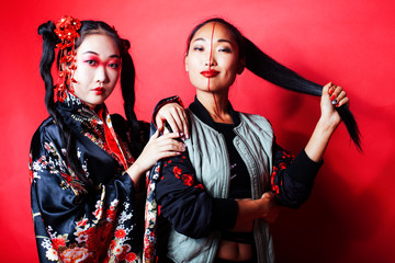 two pretty geisha girls friends: modern asian woman and traditional wearing kimono posing cheerful on red background