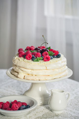 Homemade Pavlova cake with berries on the table in home interior.