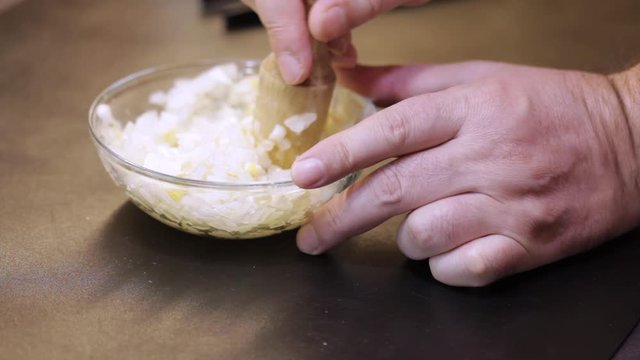 Mashing onion and garlic in a bowl with wooden pestle