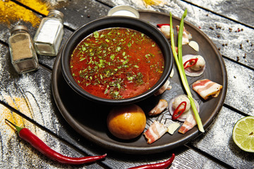 Borsch with sour cream, onions and a bun on a dark background