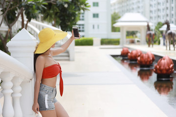 side view attractive and sexy asian girl in orange bikini with nice hat using cell phone do self portrait with happy smiling face