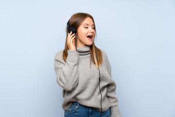 Teenager girl with sweater over isolated blue background listening to music with headphones