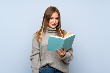 Teenager girl with sweater over isolated blue background holding and reading a book