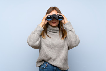 Teenager girl with sweater over isolated blue background with black binoculars