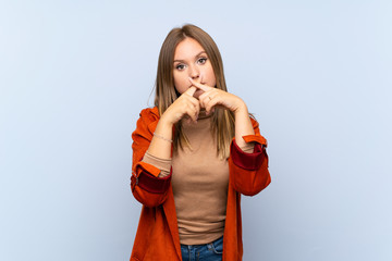 Teenager girl with coat over isolated blue background showing a sign of silence gesture