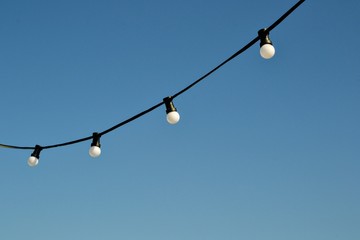 A string wire of outdoor light bulbs hanging against a clear blue sky. Light bulbs on the sky...