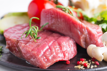 Raw beef steak on the bone with fresh vegetables in a pan on a marble background, top view