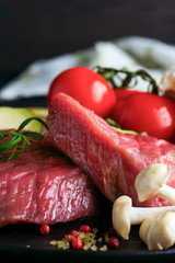 Raw beef steak on the bone with fresh vegetables in a pan on a dark stone background,