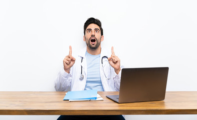 Young doctor man with his laptop over isolated wall pointing with the index finger a great idea