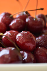 Red fresh cherries with water drops on orange background.