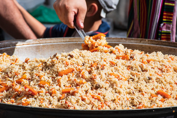 Real traditional street pilaf or plov, rice dish cooking in stock or broth, adding spices, and other ingredients such as vegetables or meat