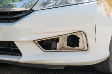 Damage to the front left bumper of a white sedan, Caused by accident.