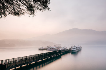Fototapeta na wymiar Beautiful tranquil landscape at Sun Moon lake in Nantao, Taiwan. Pier with boats and background of foggy mountains. Concept of peaceful, traanquility of nature.
