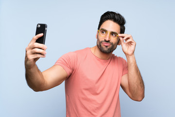 Handsome young man in pink shirt over isolated blue background making a selfie