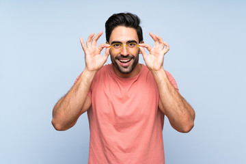 Fototapeta premium Handsome young man in pink shirt over isolated blue background with glasses and surprised
