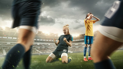 Fototapeta premium Taste or win. Young female soccer or football player in sportwear celebrating the goal in action at the stadium while gameplay. Concept of healthy lifestyle, professional sport, hobby, motion