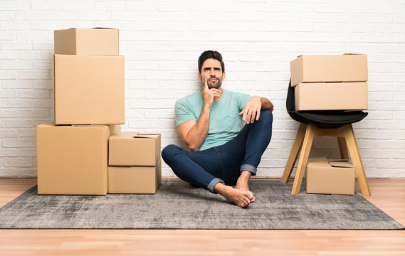 Handsome young man moving in new home among boxes thinking an idea