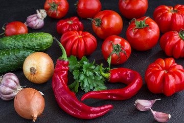 Set of vegetables on a black background: tomatoes, cucumbers, peppers, garlic, onions and parsley