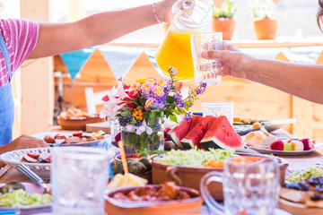 Group of hands sharing food and drink. Caucasian peoples enjoying brunch or meal together. Fruits and vegetables on the wooden table. Sunlight outdoor on the terrace