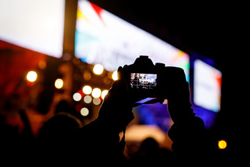 Professional dslr camera at music concert in raised up hand recording singer on a stage.