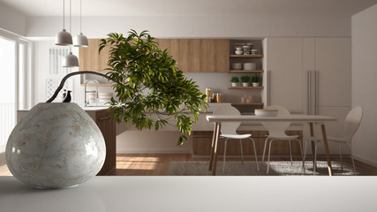 White mat table shelf with round marble vase and potted bonsai, green leaves, over minimalist kitchen with dining table, modern interior design, zen clean architecture concept idea