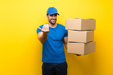 Fototapeta na wymiar Young delivery man over isolated yellow wall inviting to come with hand. Happy that you came