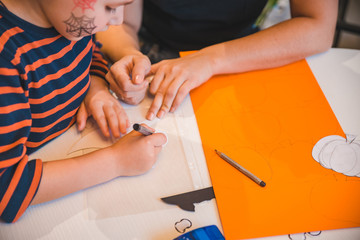 little boy with mother preparing for halloween drawing pumpkin on color paper