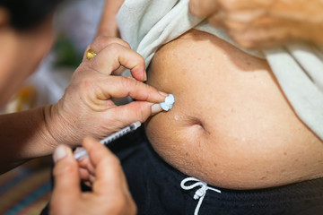 Close up of old female hand making subcutaneous insulin injection into a diabetes patient abdomen with insulin syringe at home.  