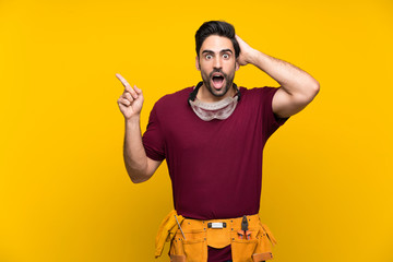 Handsome young craftsman over isolated yellow background surprised and pointing finger to the side