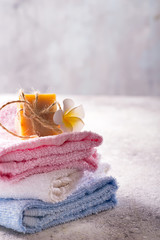 Lots of colorful bath towels stacked on each other with hand soap and flower on light stone background, copy space