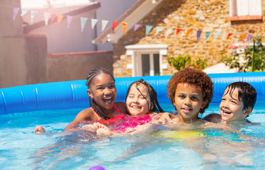 Obraz na płótnie Canvas Four happy boys, girls hug sit smile in swim pool