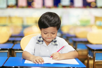 An image of Asian school boy with a pencil in left hand writes his practice happily in a classroom. Young student intent on studying. Boy concentrated in the study. 