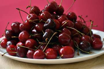 White bowl of fresh cherries on a wooden table on pink backgraund.