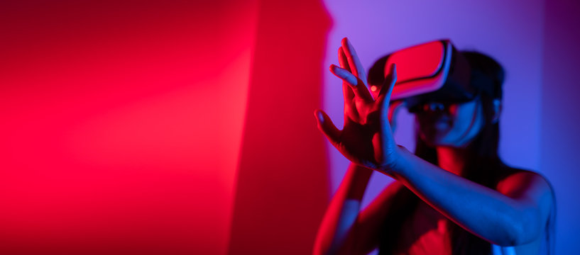 Young woman using glasses of virtual reality on dark background. Smartphone using with VR headset,virtual reality,future technology concept.Asian woman using VR glasses in colorful neon lights. - Powered by Adobe