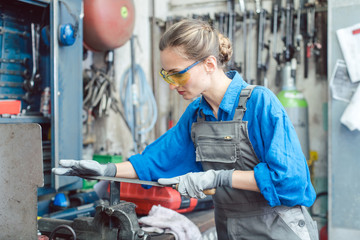 Woman worker in metal workshop deburring workpiece