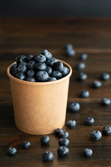 Fresh organic blueberries in a paper cup. Dark wooden table, high resolution