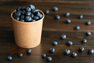 Fresh organic blueberries in a paper cup. Dark wooden table, high resolution