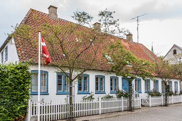 the danish flag outside a house with blue windows and a white fence in the island of Aero