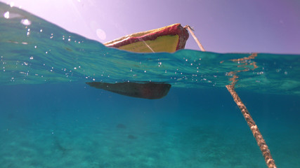 Above and below underwater photo of colourful fishing boat in turquoise clear Greek island sea