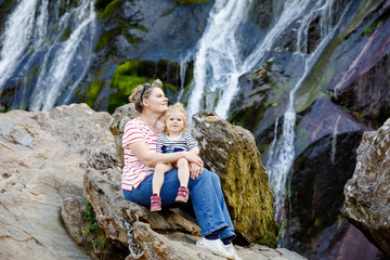 Cute toddler girl and mother sitting near water cascade of Powerscourt Waterfall, the highest...
