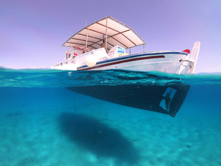 Above and below underwater photo of traditional fishing boat docked in turquoise clear sea, Mykonos...