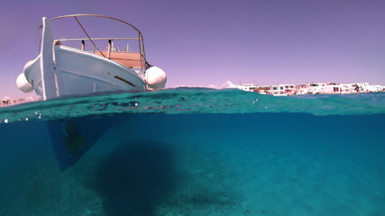 Above and below underwater photo of colourful fishing boat in turquoise clear Greek island sea