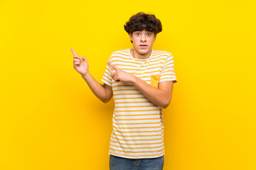 Young man over isolated yellow wall frightened and pointing to the side