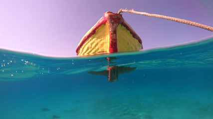 Above and below underwater photo of traditional fishing boat docked in turquoise clear sea, Mykonos island, Cyclades, Greece