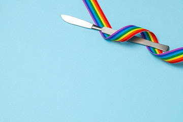 Scalpel and rainbow LGBT ribbon pride symbol. Sex change operation. Blue background. Copy space for text.