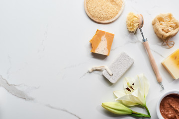 top view of natural clay mask, soap pieces, body brush, pumice stone and loofah near fresh flower...
