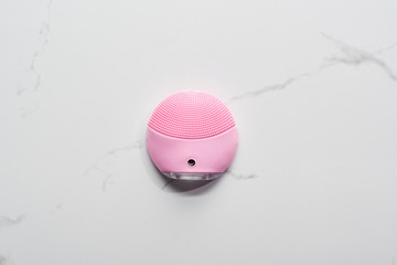 top view of pink silicone cleansing facial brush on marble surface