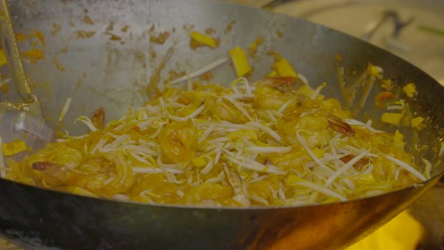 A closeup shot of a wok with vegtables and noodles inside, then sprinking the more green vegetables. 