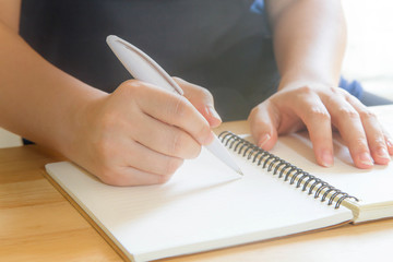 Hand writing on blank notebook with pen on wooden table