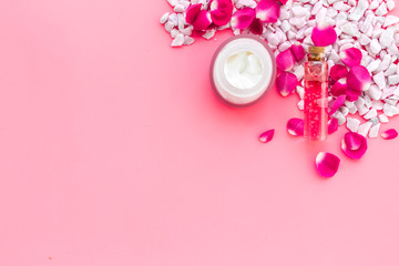 Cosmetics with sea salt and roses decoration on pink background top view space for text